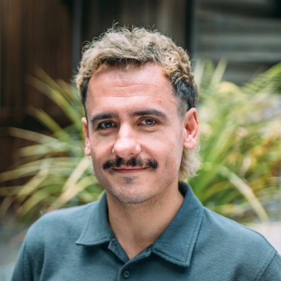 A man with a dark green polo shirt smiling and standing in front of a blurred background of ferns