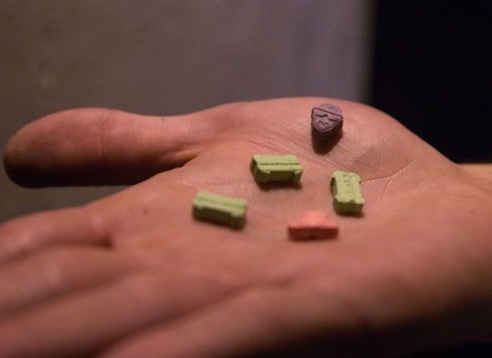 Close up of five pills on an open hand, three are green and bone shaped, one red and one purple. 