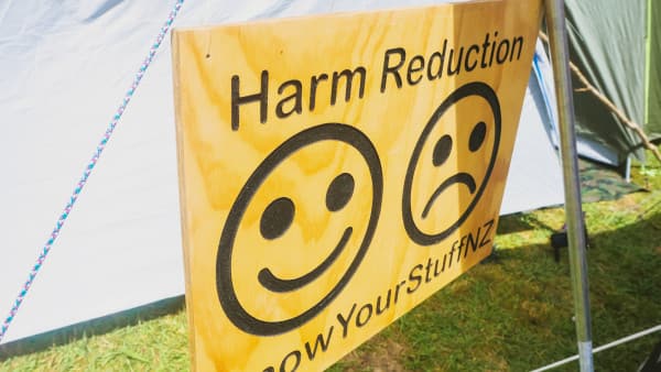 Yellow sign saying Harm Reduction Know Your Stuff NZ with a happy and sad face symbol